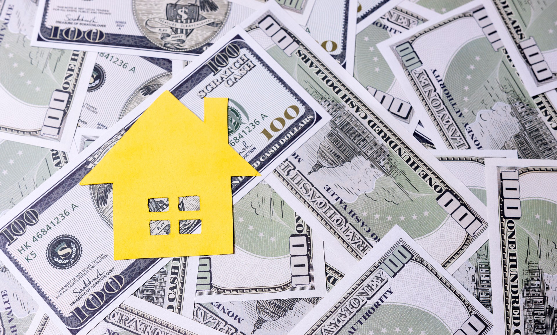 Yellow House Cutout on Pile of Hundred Dollar Bills Background