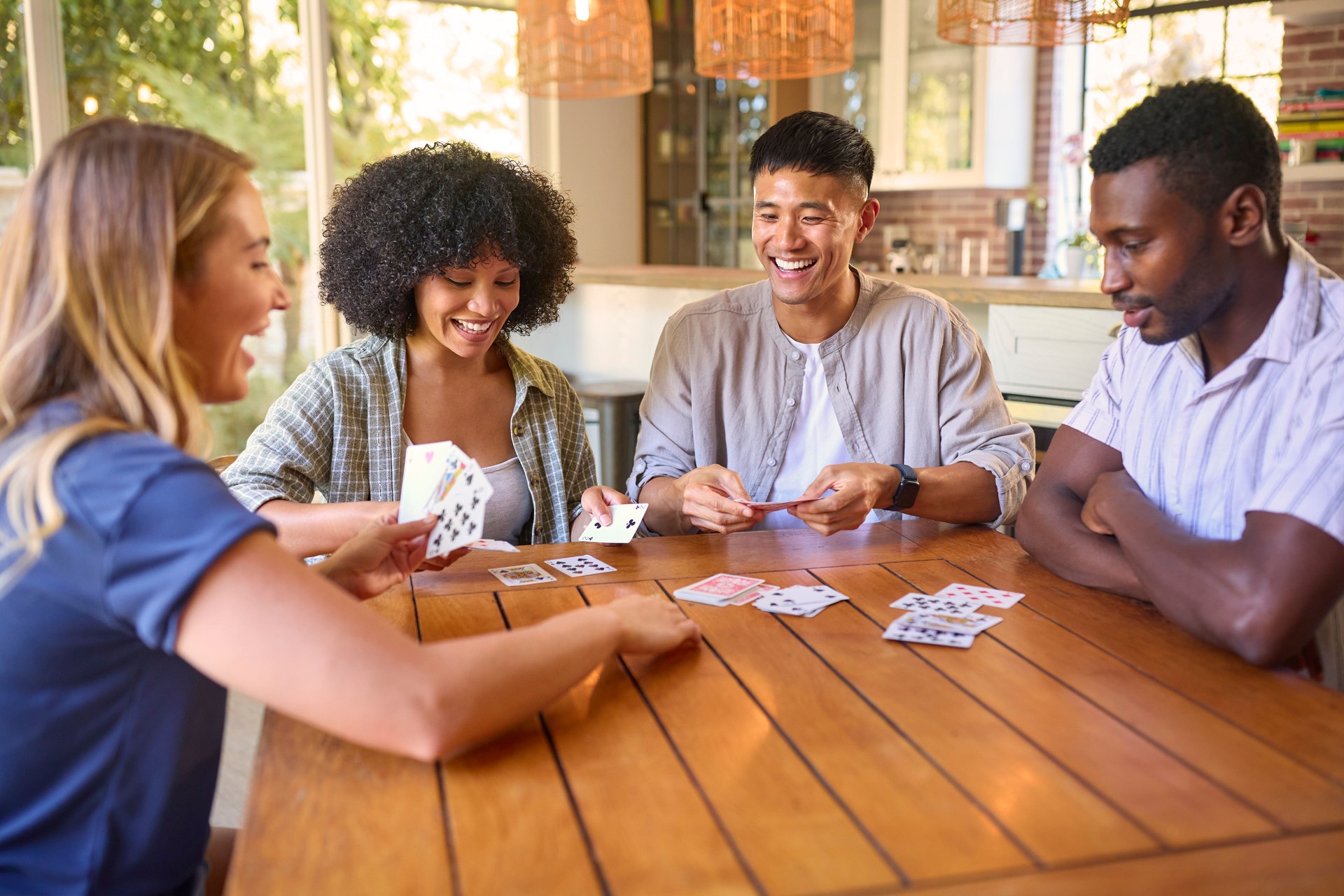 Group Of Multi-Racial Friends Sitting Around Table Playing Game Of Cards At Home Together